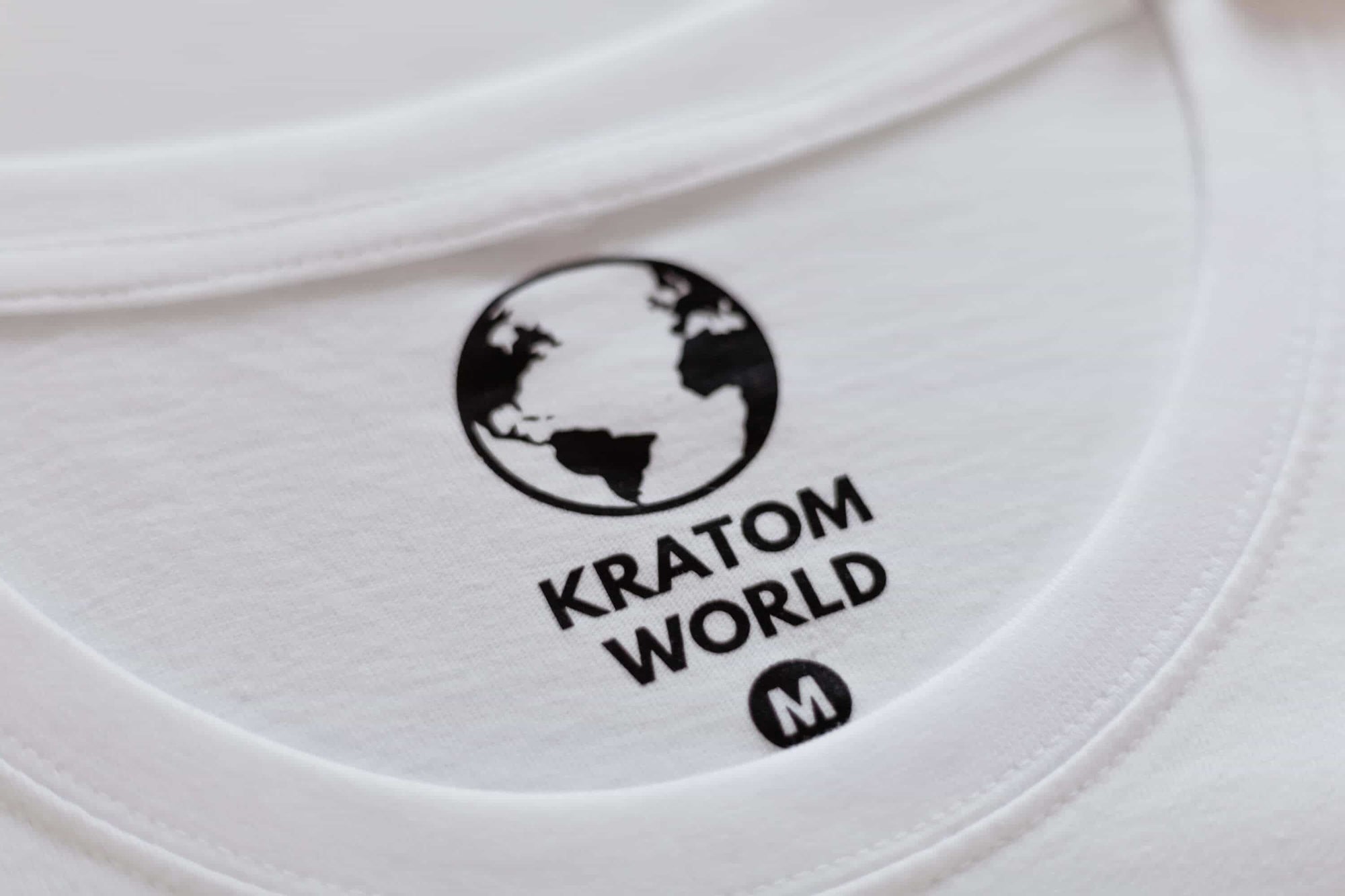 Бяла тениска Kratom World, представена в продуктов кадър като фирмена тениска с етикет.
