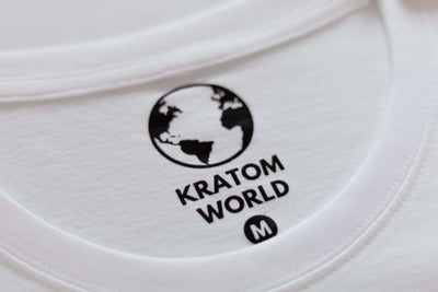 Бяла тениска Kratom World, представена в продуктов кадър като фирмена тениска с етикет.